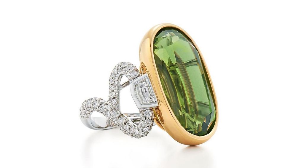 Центральный перидот весом 31 карат обрамлен парой бриллиантов в форме щита и установлен на изогнутой шинке, инкрустированной бриллиантами круглой огранки